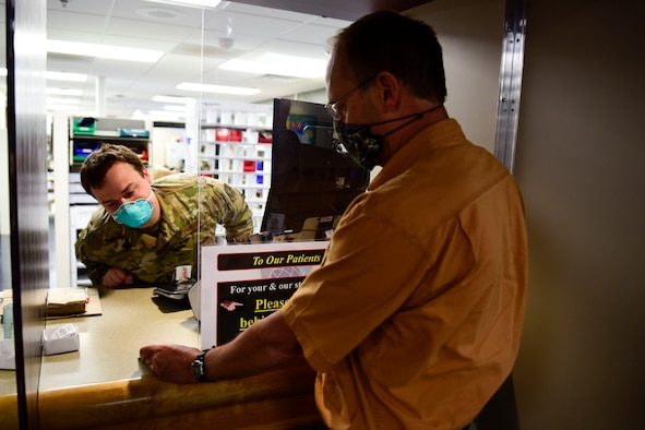 Staff Sgt. Sean Rourke (pictured left), 92nd Medical Support Squadron pharmacy technician, demonstrates a ‘hands-off’ approach for pharmacy technicians to verify a beneficiaries military identification card, May 29, 2020, at Fairchild Air Force Base, Wash. This verification technique, amongst other safety precautions, was put in place to aid in preventing the potential spread of the 2019 Coronavirus to keep pharmacy staff and patients safe. (U.S. Air Force photo by Staff Sgt. Nick J. Daniello)