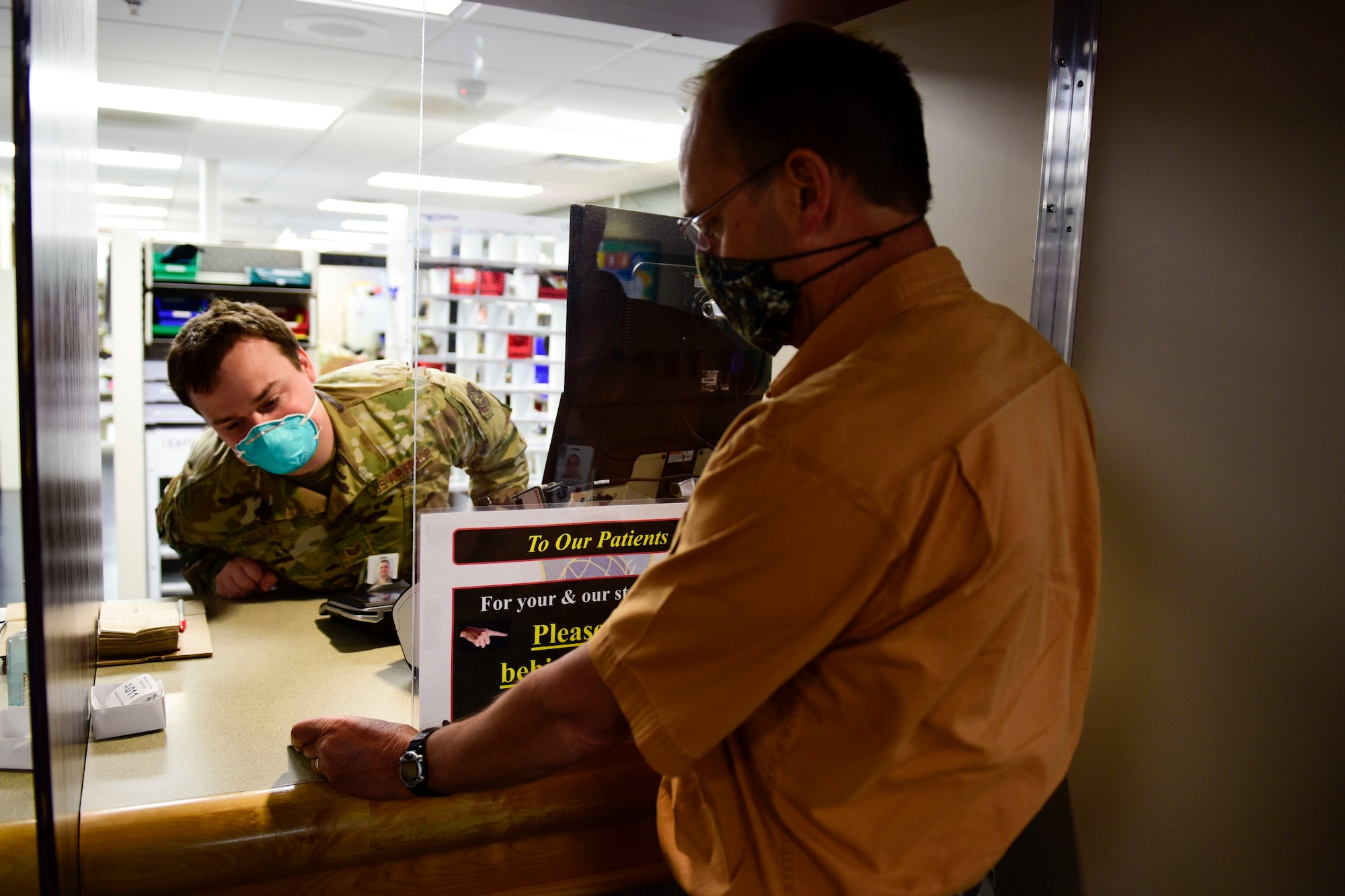 Staff Sgt. Sean Rourke (pictured left), 92nd Medical Support Squadron pharmacy technician, demonstrates a ‘hands-off’ approach for pharmacy technicians to verify a beneficiaries military identification card, May 29, 2020, at Fairchild Air Force Base, Wash. This verification technique, amongst other safety precautions, was put in place to aid in preventing the potential spread of the 2019 Coronavirus to keep pharmacy staff and patients safe. (U.S. Air Force photo by Staff Sgt. Nick J. Daniello)
