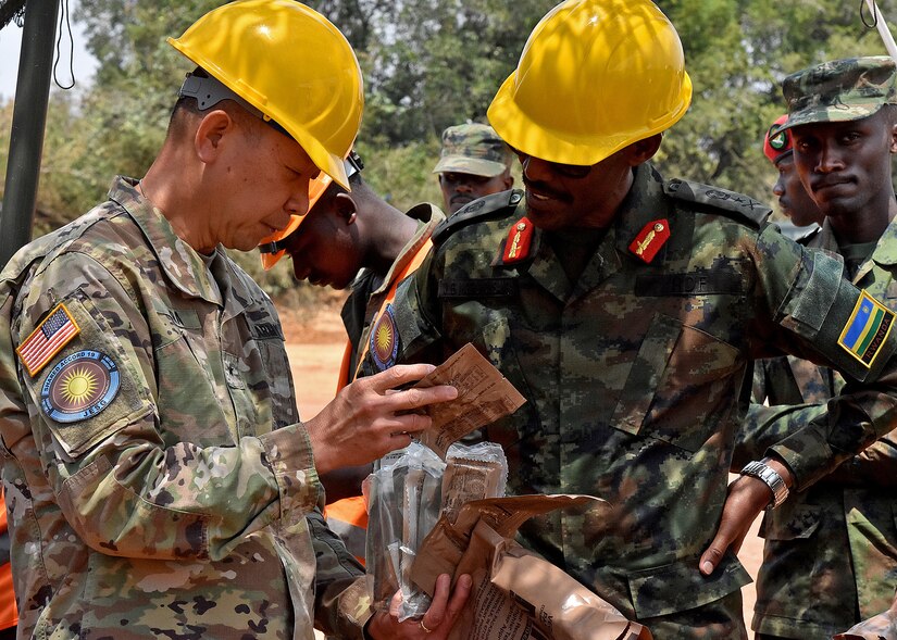 U.S. Army Brig. Gen. Lapthe C. Flora, deputy commanding general for U.S. Army Africa, left, shows Rwanda Defence Force Brig. Gen. John Baptist Ngiruwonsanga, exercise co-director, center, the choices inside a meal ready to eat (MRE) during a visit to exercise participants at the Exercise Shared Accord 2019