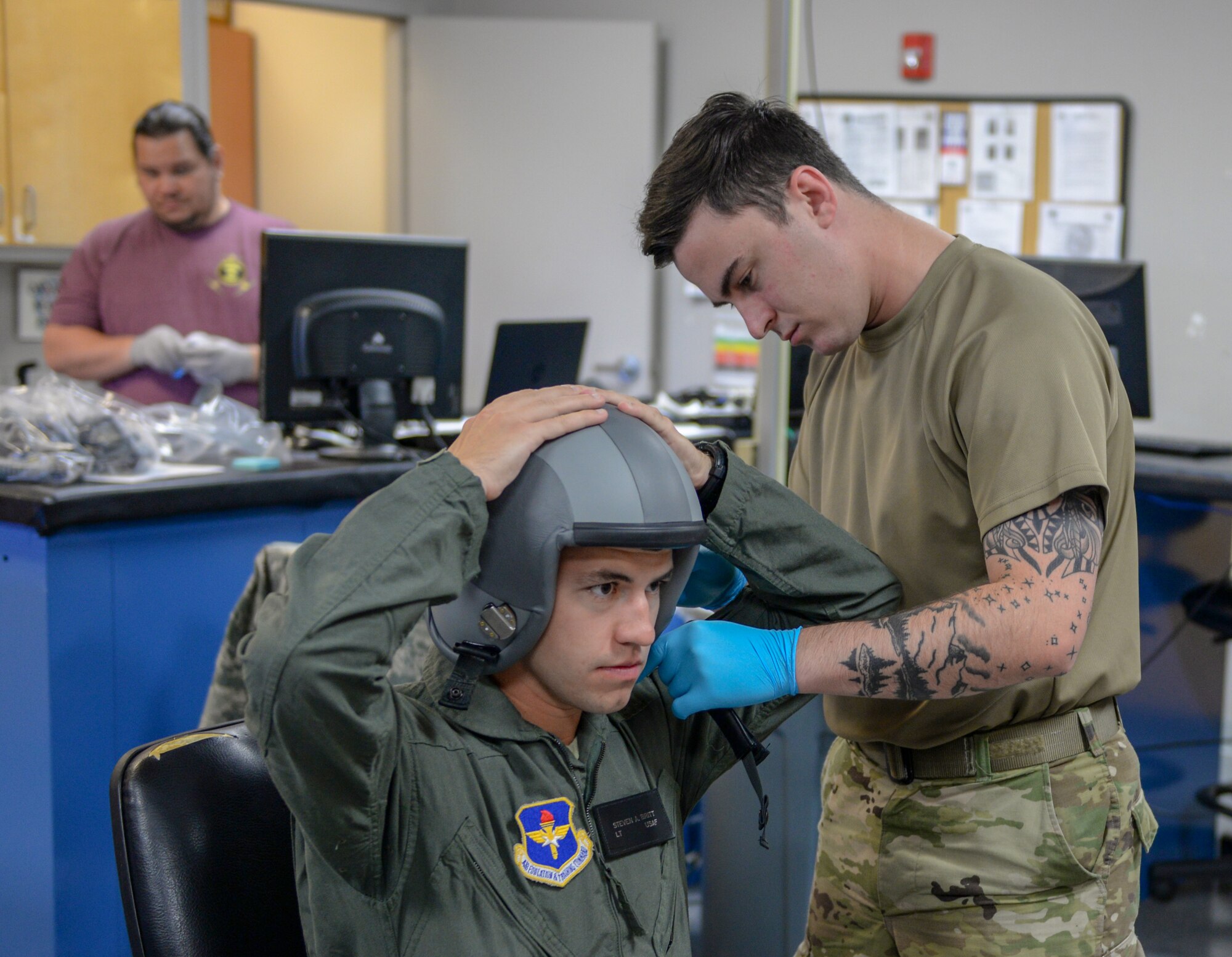 Second Lt. Steven Britt, 37th Flying Training Squadron student pilot, holds down a helmet, while Senior Airman Dillon Arizta, 37th FTS Aircrew Flight Equipment specialist, attaches a chinstrap on June 10, 2020, at Columbus Air Force Base, Miss. While in phase two of Specialized Undergraduate Pilot Training at the 37th FTS, student pilots will train in the T-6A Texan II.   (U.S. Air Force photo by Airman 1st Class Davis Donaldson)