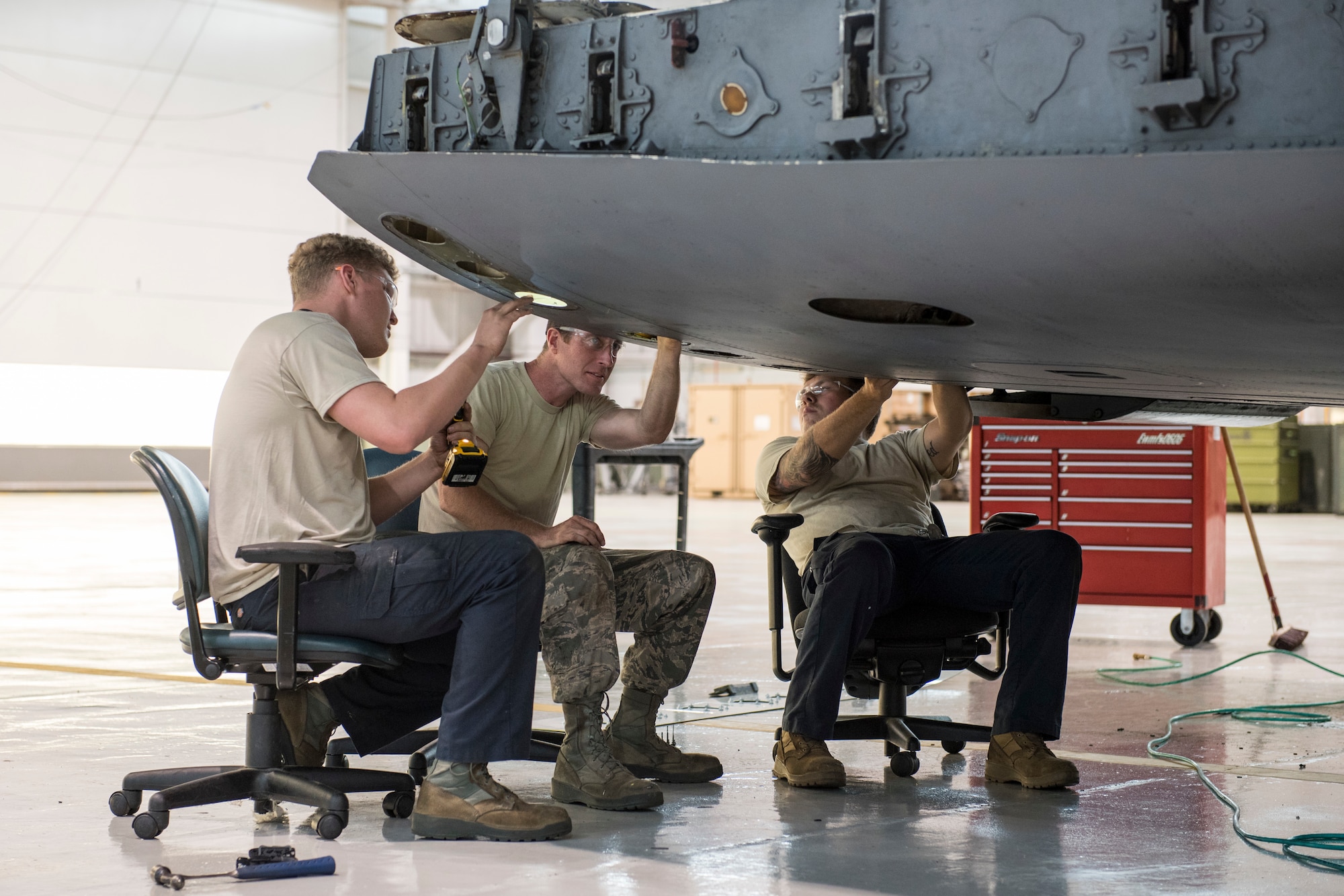 Tech Sgt. Daniel Barrow, Staff Sgt. Doug Miller and Staff Sgt. Kevin Cecil sit in office chairs, just the right height to comfortably repair damage to the cargo ramp on a C-17 Globemaster III aircraft at the 167th Airlift Wing, Martinsburg, W.Va., May 28, 2020.