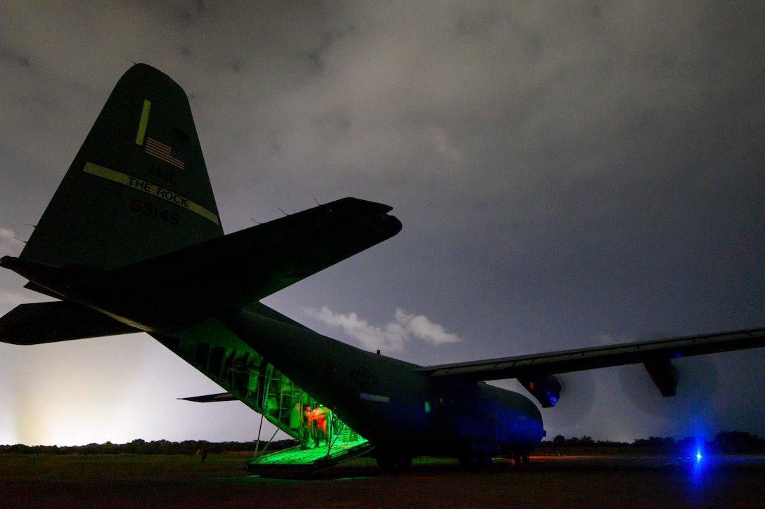 An aircraft sits on a runway illuminated by blue and green lights.