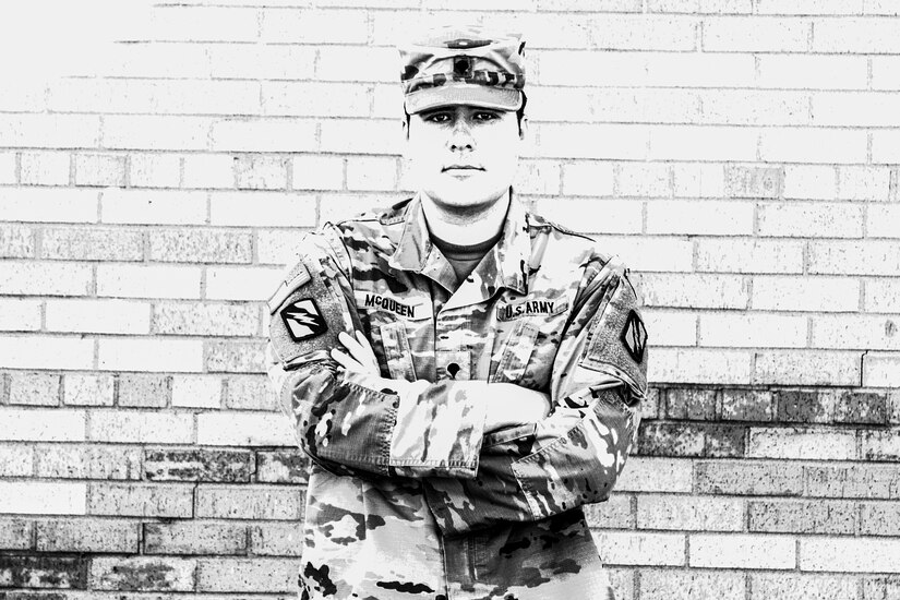 A soldier poses with his arms crossed over his chest in front of a brick wall.