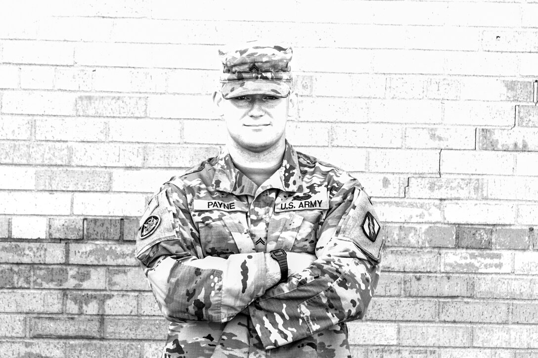 A soldier poses with his arms crossed over his chest in front of a brick wall.