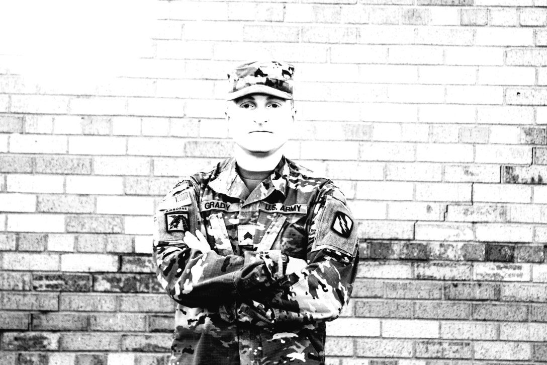 A soldier poses with his arms crossed over his chest in front of a brick wall.