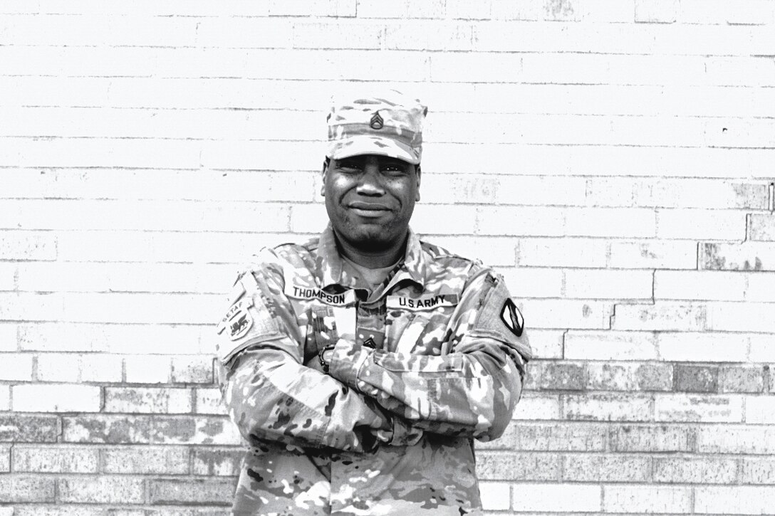 A soldier poses with his arms crossed over his chest in front of a brick wall.