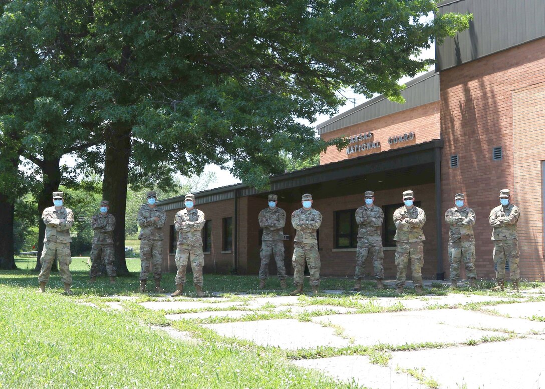 Ten soldiers with masks on stand in a yard in front of a building.