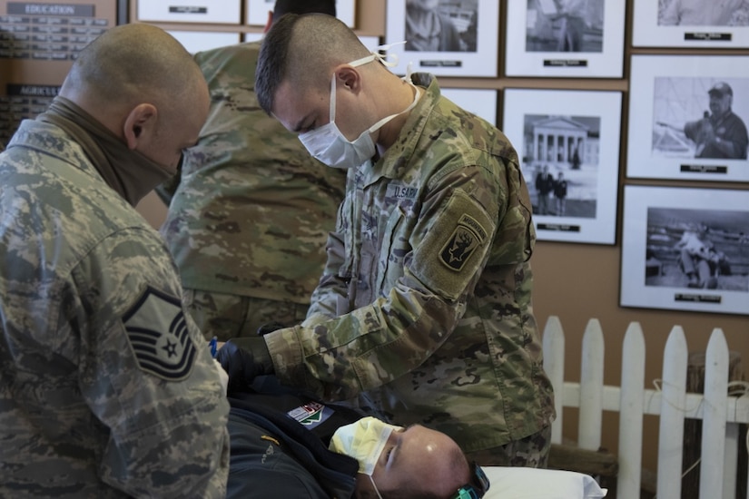Two national guardsmen wearing masks treat a patient also wearing a mask.