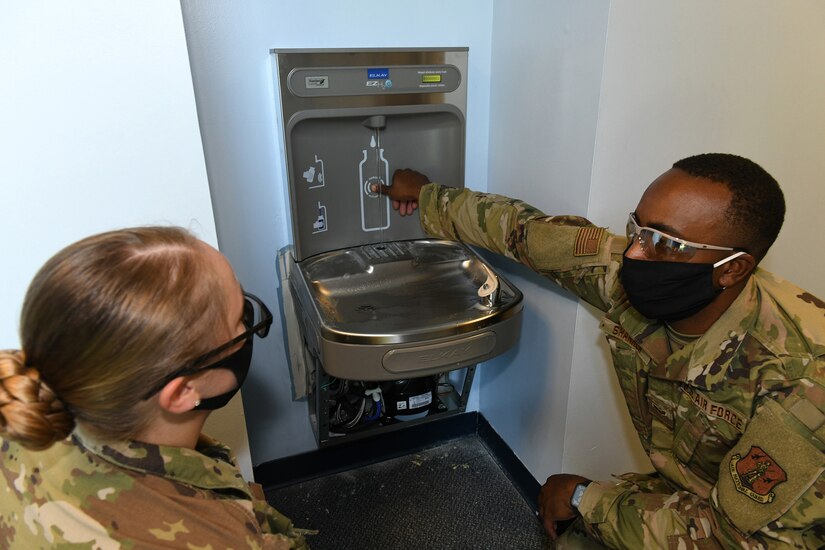 Photo shows two Airmen setting off a bottle sensor on a water fountain.
