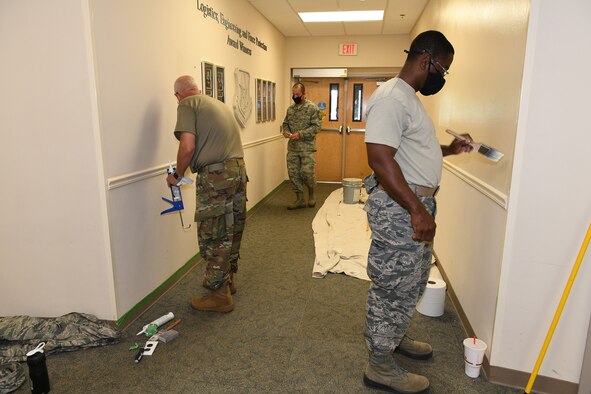 Photo shows three Airmen painting walls in a hallway.