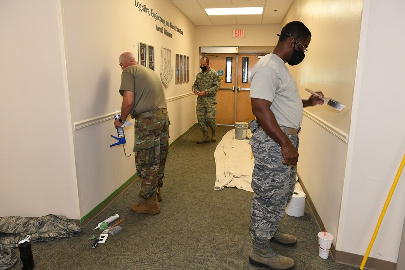 Photo shows three Airmen painting walls in a hallway.