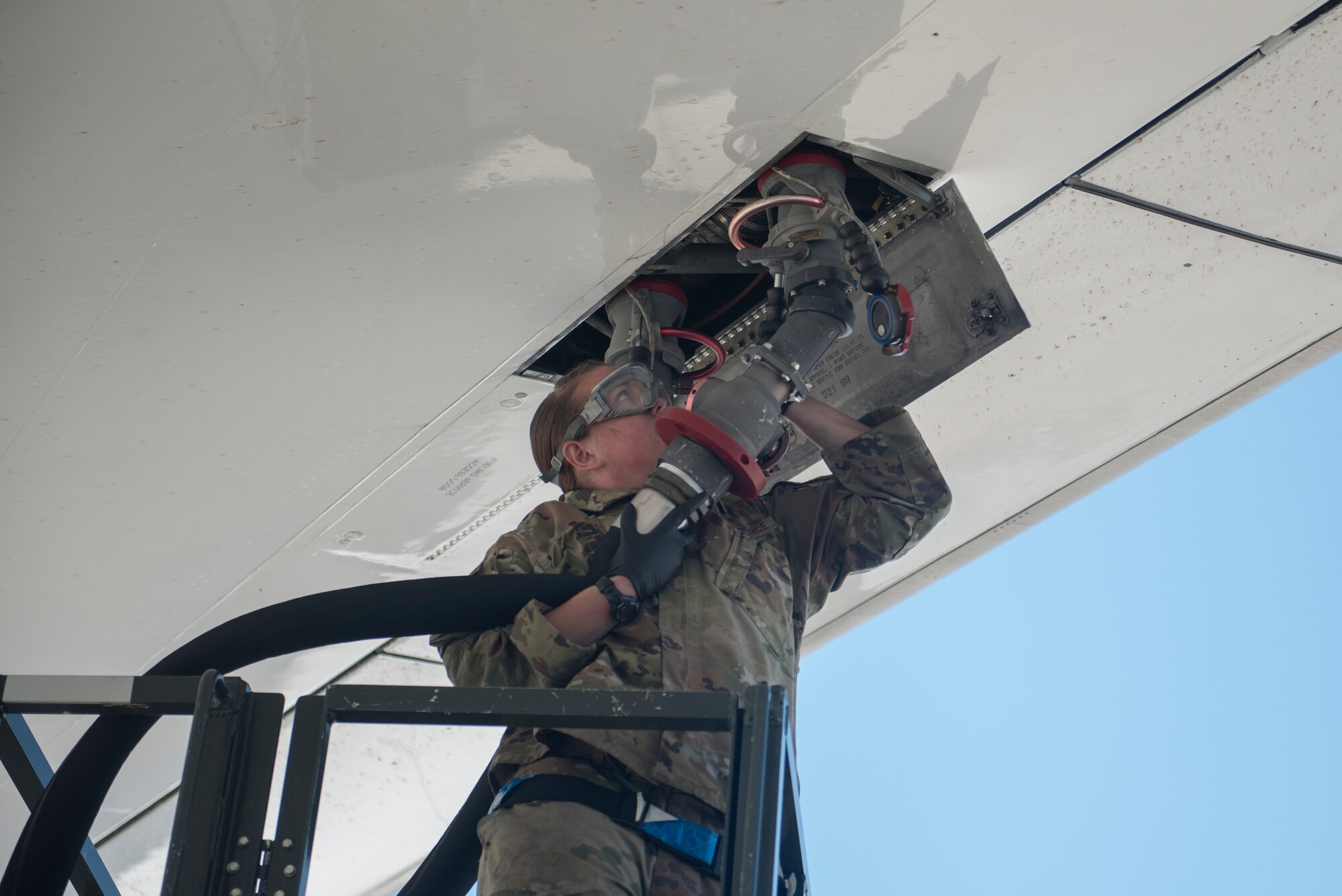 an Airman connects a large hose to an aircraft.