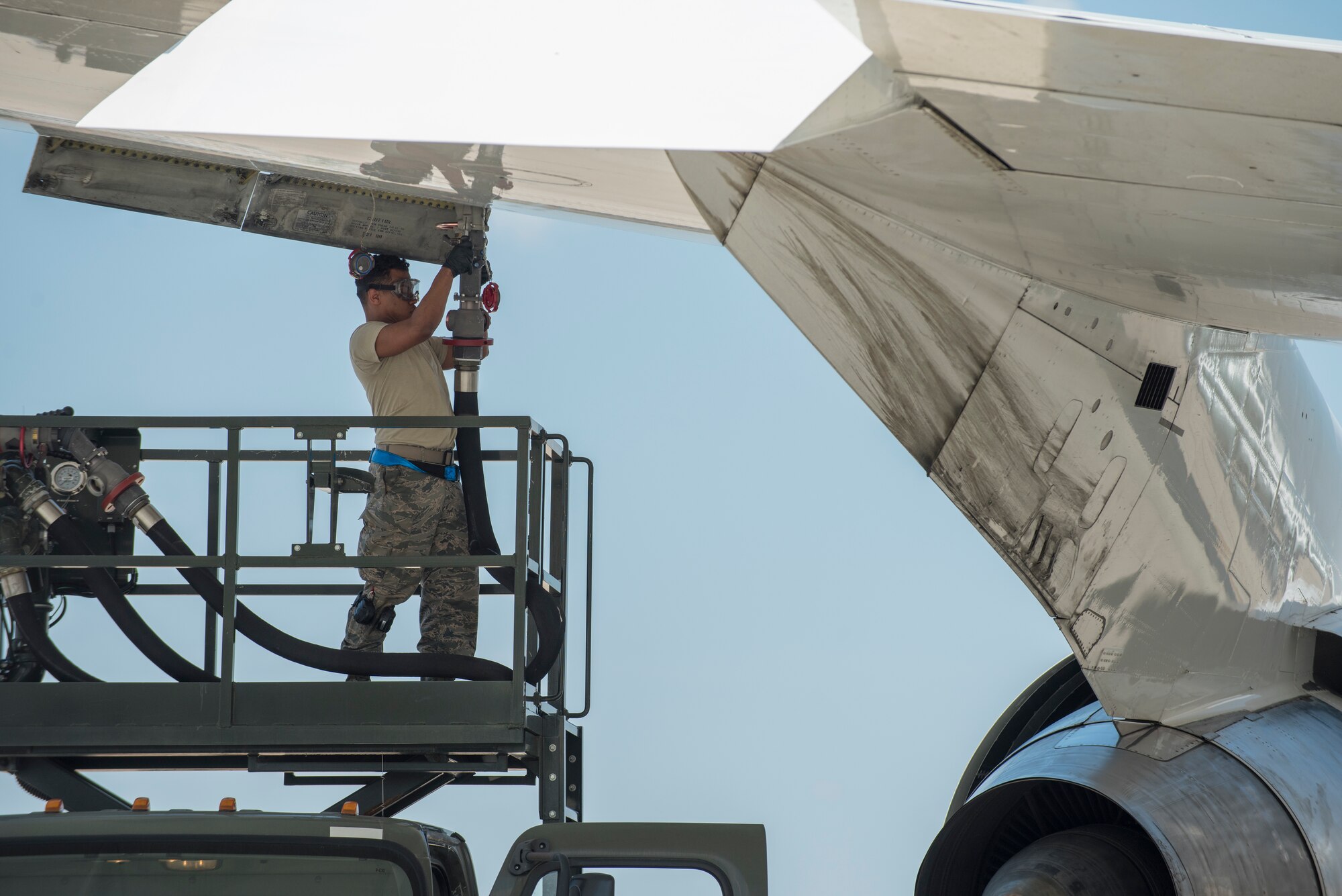 an airman connects a large fueling hose to an aircraft.