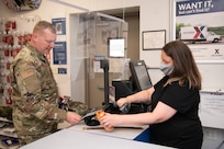 Angela Taber, 167th Airlift Wing base exchange store cashier, stands behind a plexiglass shield while scanning Staff. Sergeant Corey Kershner's items at the 167th Airlift Wing, Martinsburg, W. Va., June 11, 2020. Airmen returned to base for the first unit training assembly in two months, after regularly-scheduled training events were cancelled in April and May because of COVID-19 precautions. Airmen are using, homemade masks, social distancing, staggered schedules, and plexiglass barriers to defend themselves from the virus.