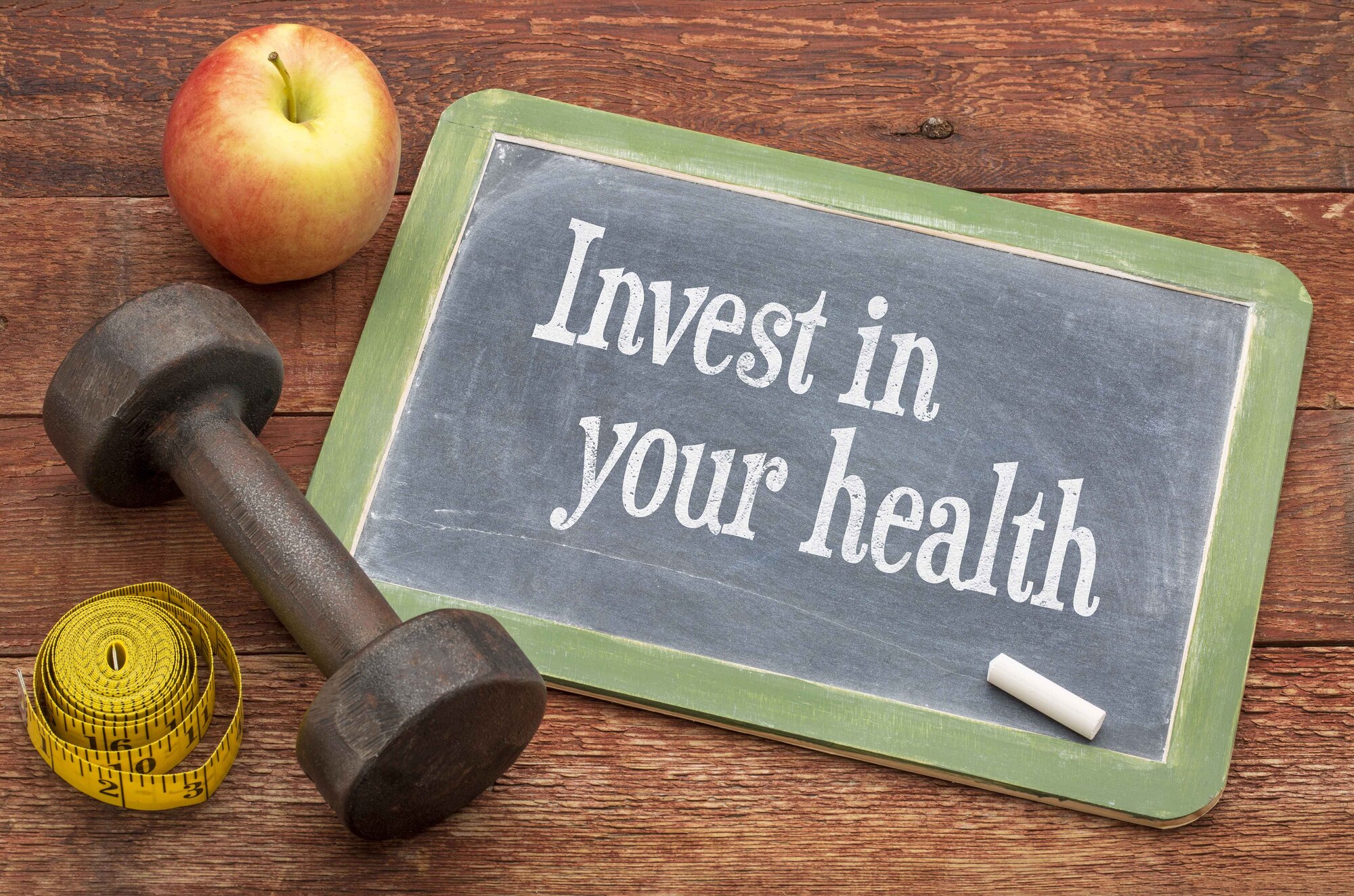 Graphic says "Invest in your health" written on a small chalkboard and has a dumb bell, measuring tape and apple next to it.
