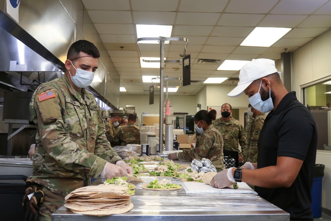 Soldiers wearing protective gear prepare meals in a kitchen.