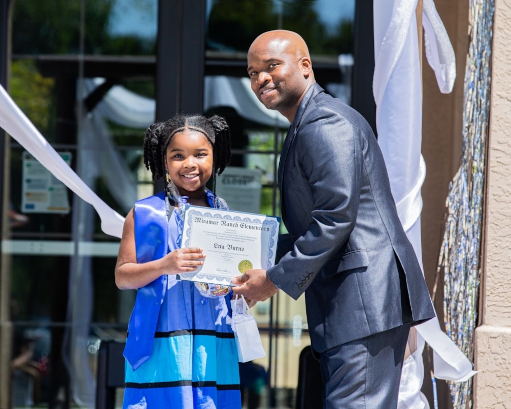 Leia Burns, an elementary graduate from Miramar Ranch Elementary, receives her certificate from Isiah Burns, her father, at the Milcon Clubhouse on Marine Corps Air Station Miramar, California, June 13, 2020. Elizabeth Burns, the mother of Leia and Isiah’s spouse, orchestrated the special graduation to give students a chance to celebrate their achievement after schools cancelled their graduations due to the pandemic, and included procedures and restrictions in place to prevent COVID-19 transmission. (U.S. Marine Corps photo by Lance Cpl. Cheng Chang/Released)