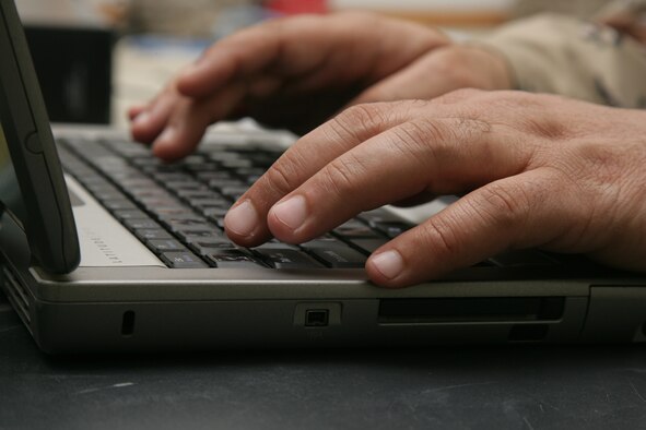 A service member types at a laptop keyboard.