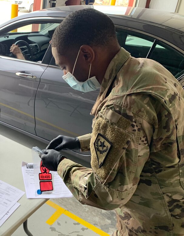 A soldier wearing a face mask places a medical sample into a plastic bag.