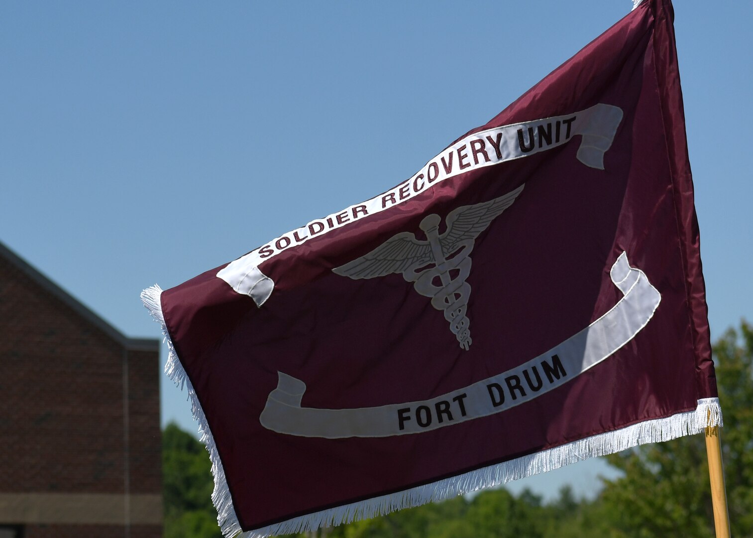 The newly uncased flag of the Fort Drum Soldier Recovery Unit (SRU) flies in front of the SRU headquarters building following a re-designation ceremony on Fort Drum, N.Y. June 16, 2020.