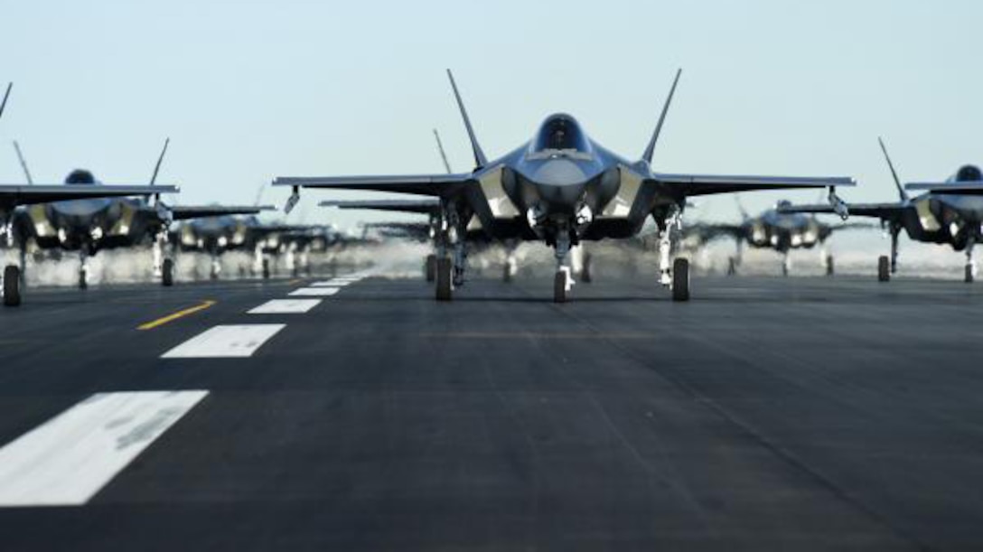 Rows of F-35 jets sit on pavement shimmering with heat