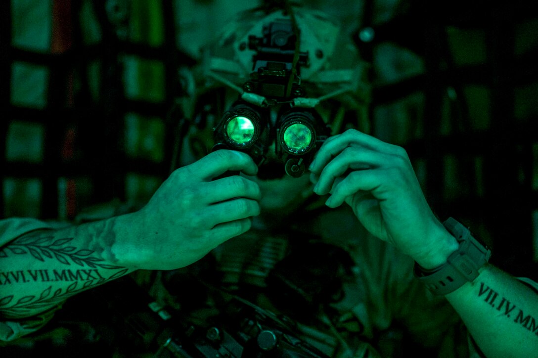 A soldier illuminated by green light adjusts eyewear he's wearing.