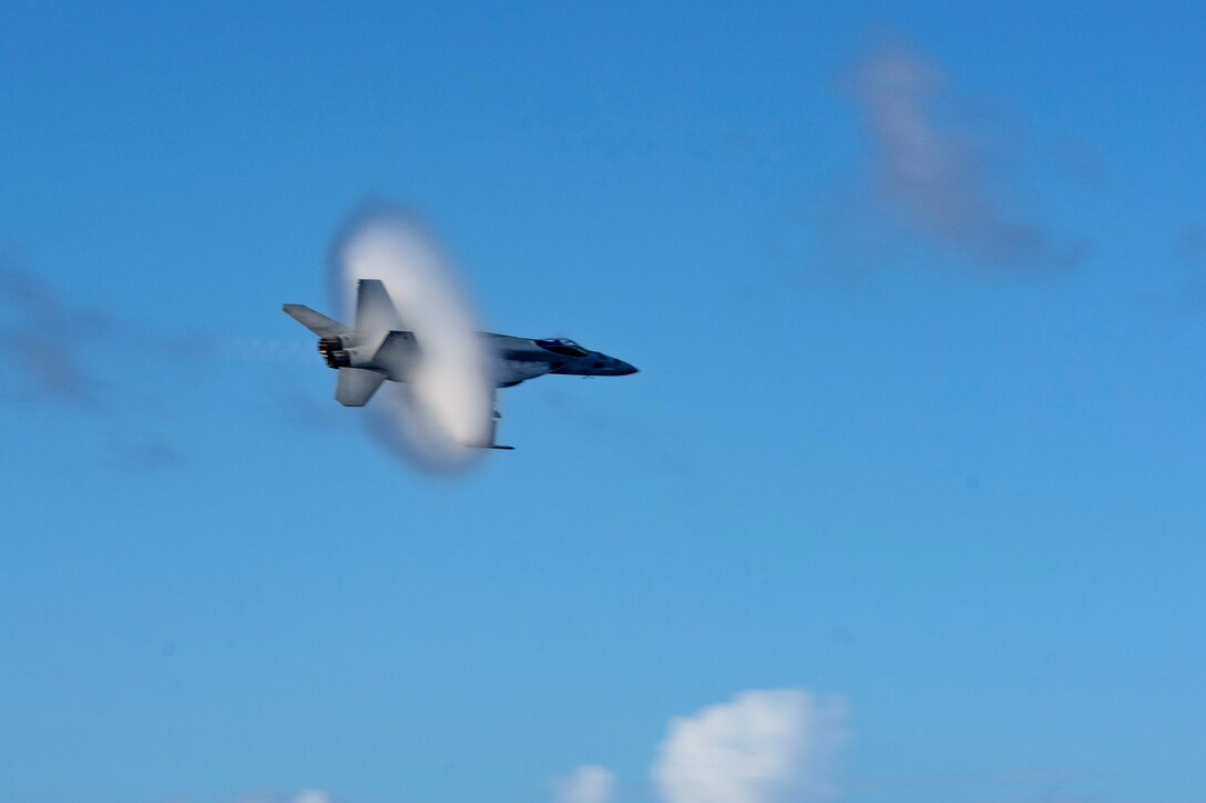 A smoke hoop surrounds a jet flying in the sky.