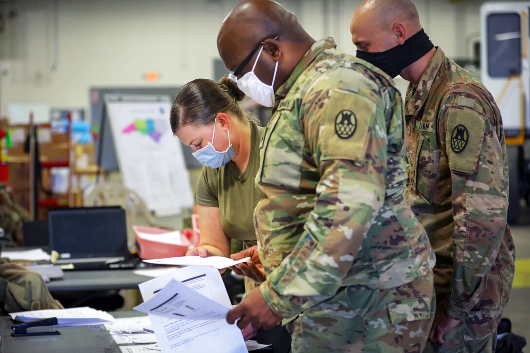 Three service members review some documents inside a warehouse.