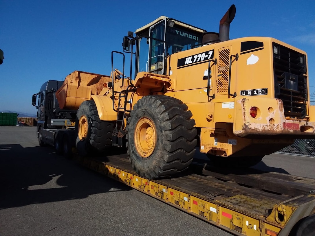 A scoop loader on a flatbed tractor trailer.