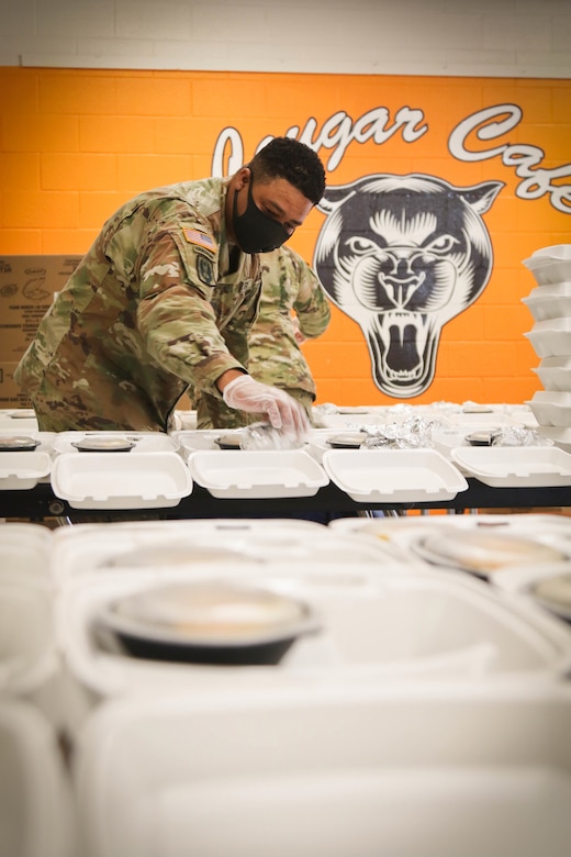 A soldier wearing a face mask assembles packaged meals.