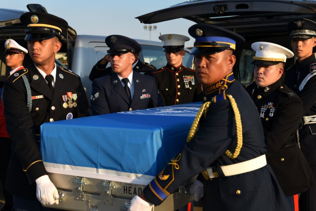 Service members carry a metal box that is draped with a United Nations flag.