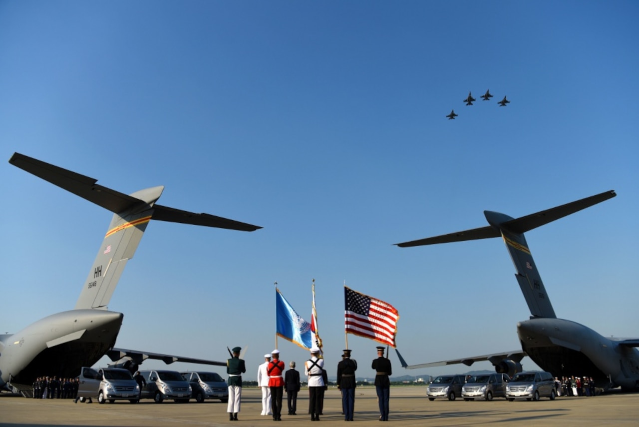 An honor guard stands by boxes of remains draped with United Nations flags on a military cargo plane.