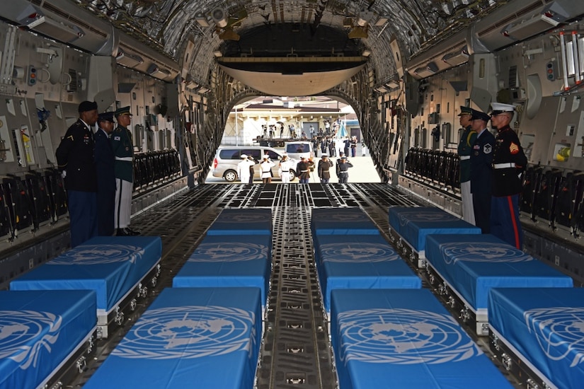 An honor guard stands by boxes of remains draped with United Nations flags on a military aircraft.