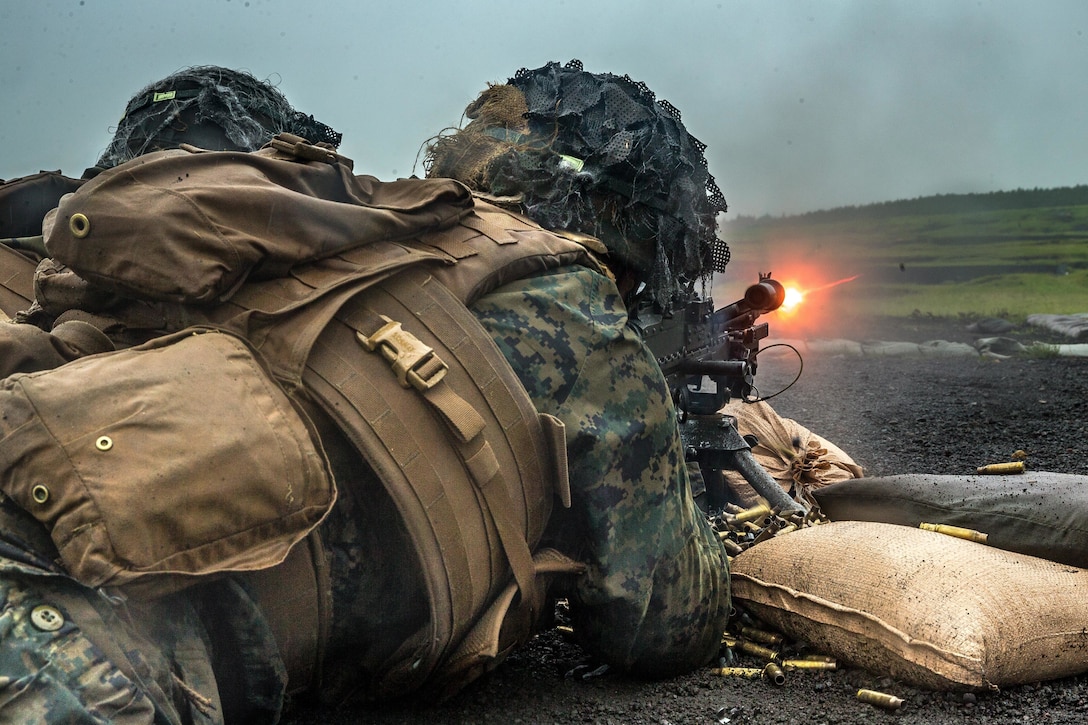 A Marine fires a machine gun while lying on the ground.