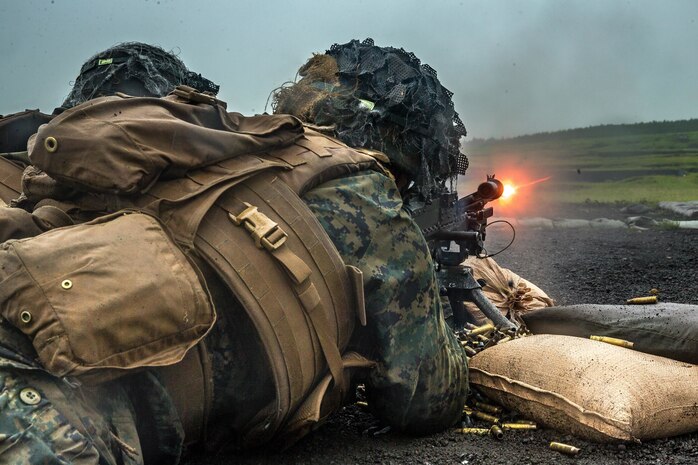 A Marine fires a machine gun while lying on the ground.