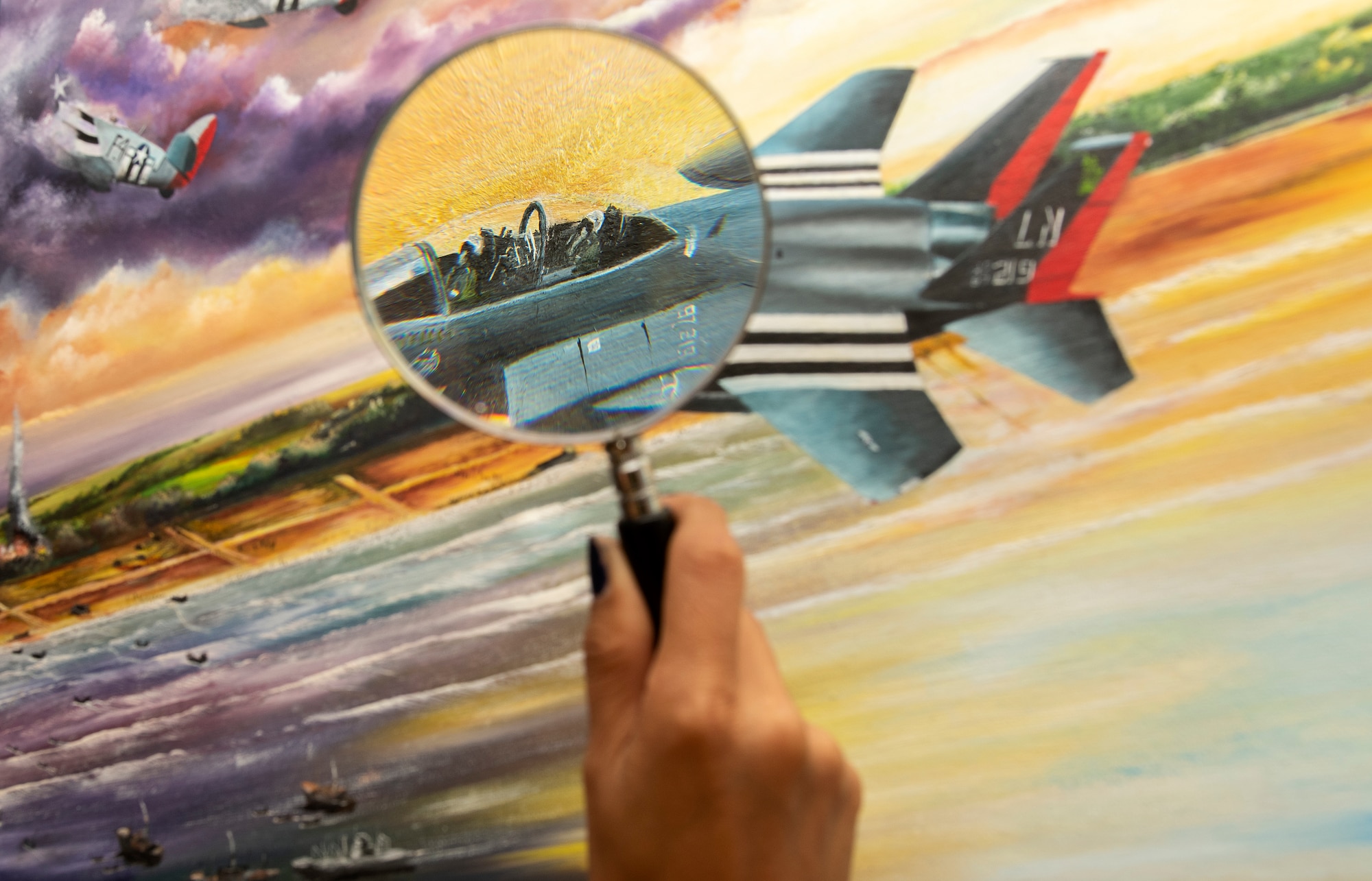 Fine details can be seen through a magnifying glass on a painting presented on behalf of Colin Mason, 48th Mission Support Group Honorary commander, and his wife Elizabeth, to the 48th Fighter Wing at Royal Air Force Lakenheath, England, June 19, 2020. The painting is a tribute to 48th FW history and it’s involvement in D-Day at Normandy, France during World War II. (U.S. Air Force photo by Airman 1st Class Jessi Monte)
