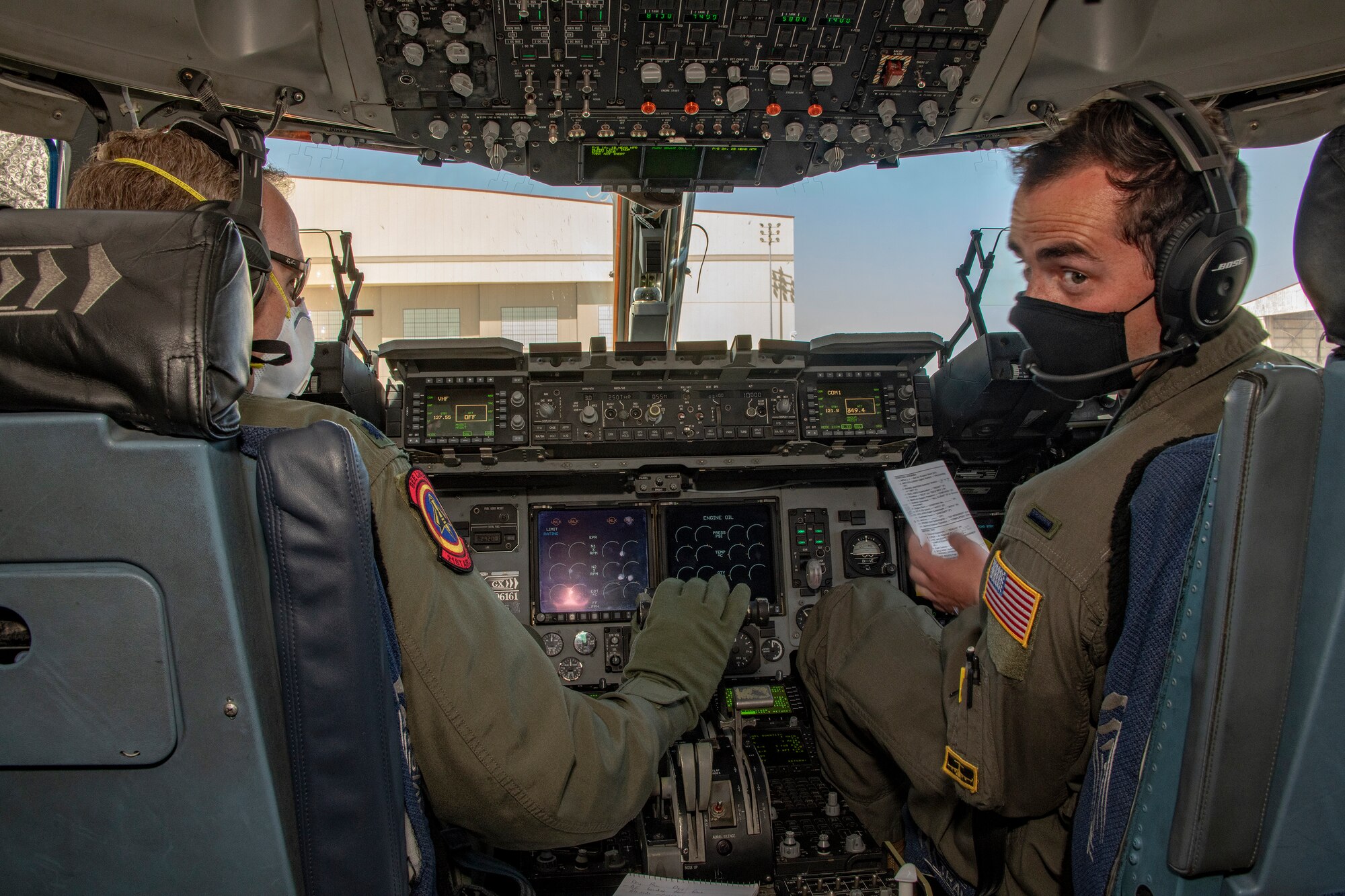 U.S. Air Force Lt. Col Michael Pettibone, left, and 1st Lt. John Massey, 21st Airlift Squadron pilots, conduct preflight operations in the flight deck of a C-17 Globemaster III May 6, 2020, at Travis Air Force Base, California. Aircrews have adapted to meet Department of Defense requirements to minimize the spread of the coronavirus and to prioritize health and safety by using personal protective equipment and sanitizing flight controls. (U.S. Air Force photo by Heide Couch)