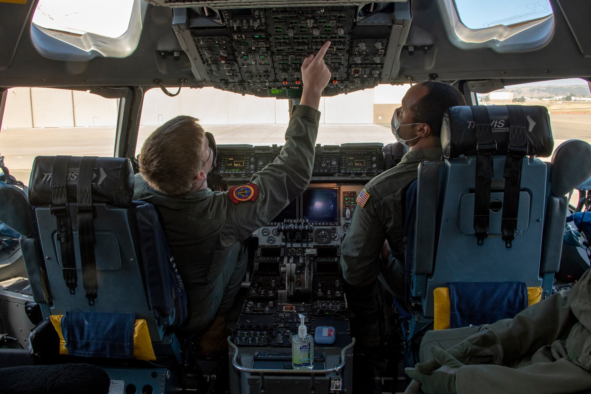 U.S. Air Force Airman 1st Class Eric Vanderford, left, 21st Airlift Squadron loadmaster, and Master Sgt. Jesse Williams, 21st AS instructor loadmaster, conduct preflight operations in the flight deck of a C-17 Globemaster III May 6, 2020, at Travis Air Force Base, California. Aircrews have adapted to meet Department of Defense requirements to minimize the spread of the coronavirus and to prioritize health and safety by using personal protective equipment and sanitizing flight controls. (U.S. Air Force photo by Heide Couch)