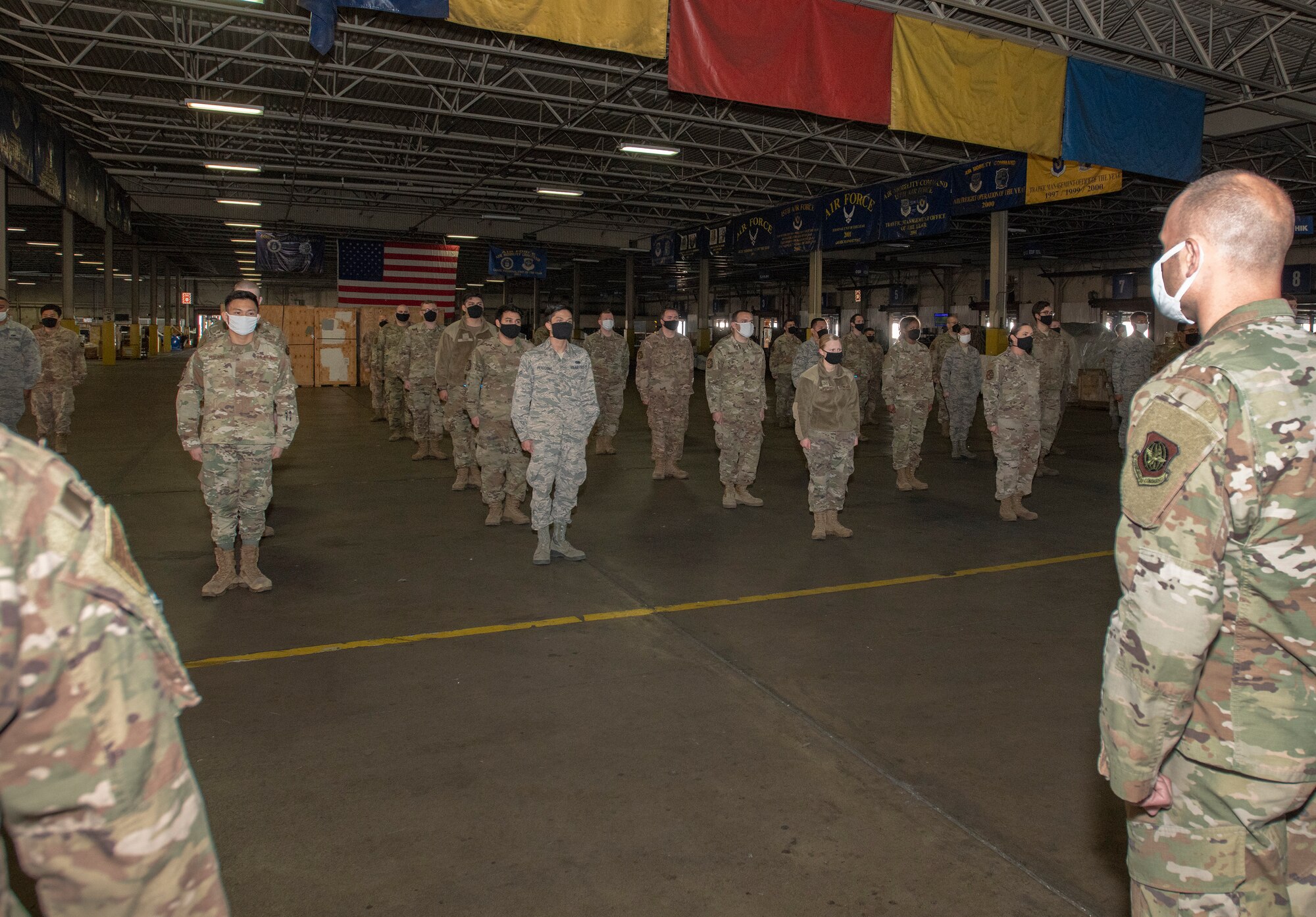 U.S. Airmen assigned to the 60th Aerial Port Squadron, stand in formation during an early morning roll call June 4, 2020, at Travis Air Force Base, California. The 60th APS continue to coordinate and deliver goods and services while enforcing the physical distancing and hygiene safety measures in place to help mitigate the spread of COVID-19. (U.S. Air Force photo by Heide Couch)