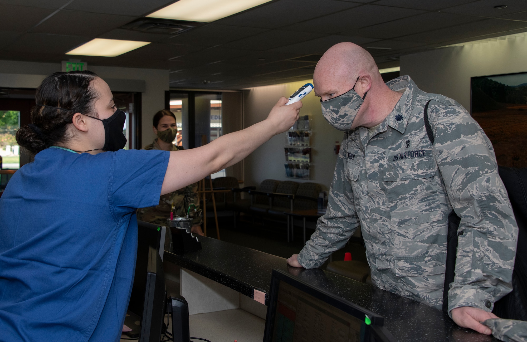 U.S. Air Force Airman 1st Class Kiarra Vendrell, left, 60th Dental Squadron dental technician, takes the temperature of Lt. Col. Thomas Weber, right, 60th DS dentist, June 6, 2020, at Travis Air Force Base, California. Dental clinic staff and patients are screened for COVID-19 symptoms prior to reporting to duty or appointments. (U.S. Air Force photo by Heide Couch