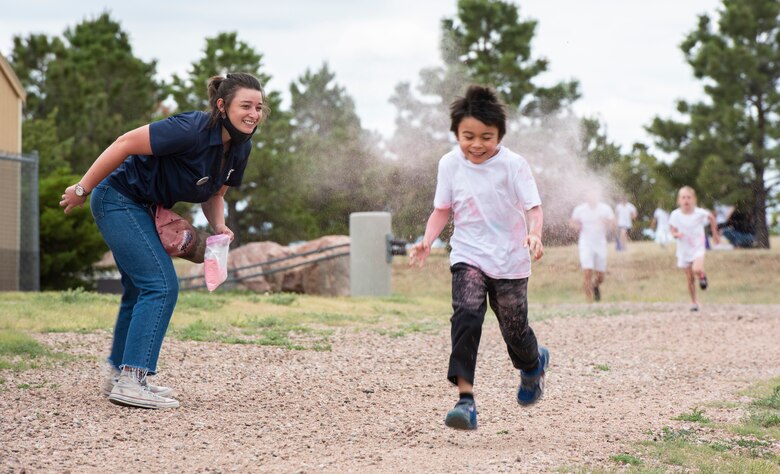Katherine Jurgensen, School Age Care program assistant, left, tosses colored cornstarch at William, 8, during the School Age Program Color Run at Schriever Air Force Base, Colorado, June 19, 2020. Due to COVID-19 restrictions, the SAC staff hasn’t been able to plan any field trips. They organized the run to provide the children an opportunity to have fun outdoors. (U.S. Air Force photo by Airman 1st Class Amanda Lovelace)