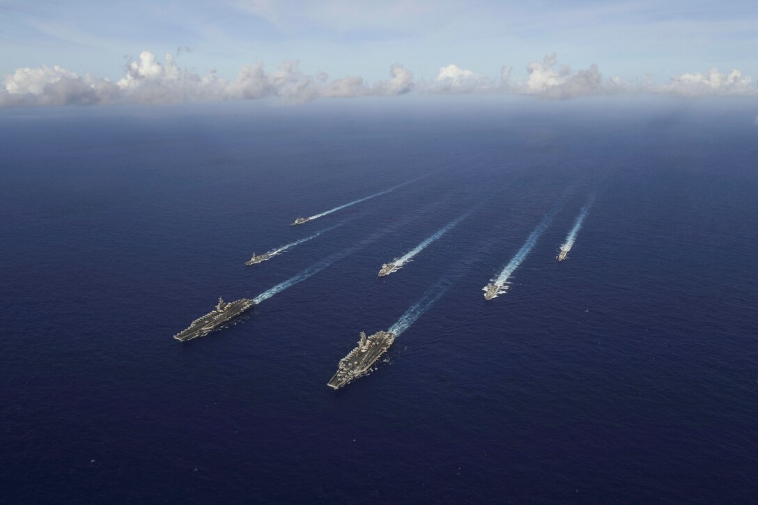 Navy ships travel a body of water.