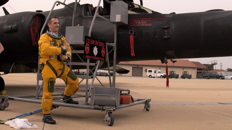 Lt. Col Georgescu stands with one foot on the stepping ladder next to the U-2 while releasing the cork from a bottle of champagne.