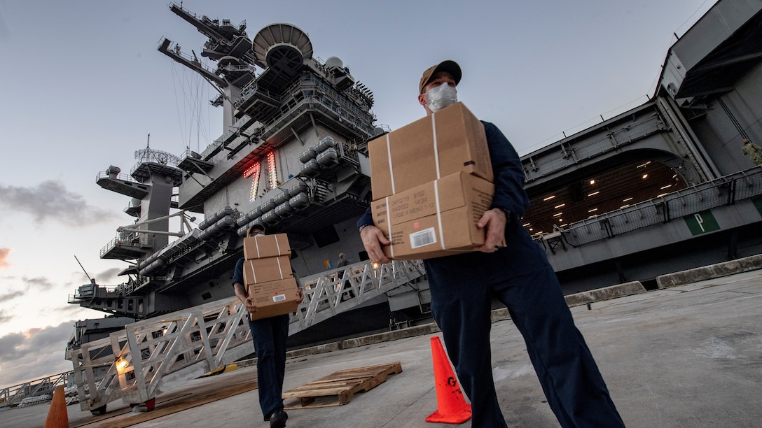Sailors wearing masks receive boxes of Meals, Ready to Eat, for those quarantined on the USS Theodore Roosevelt.