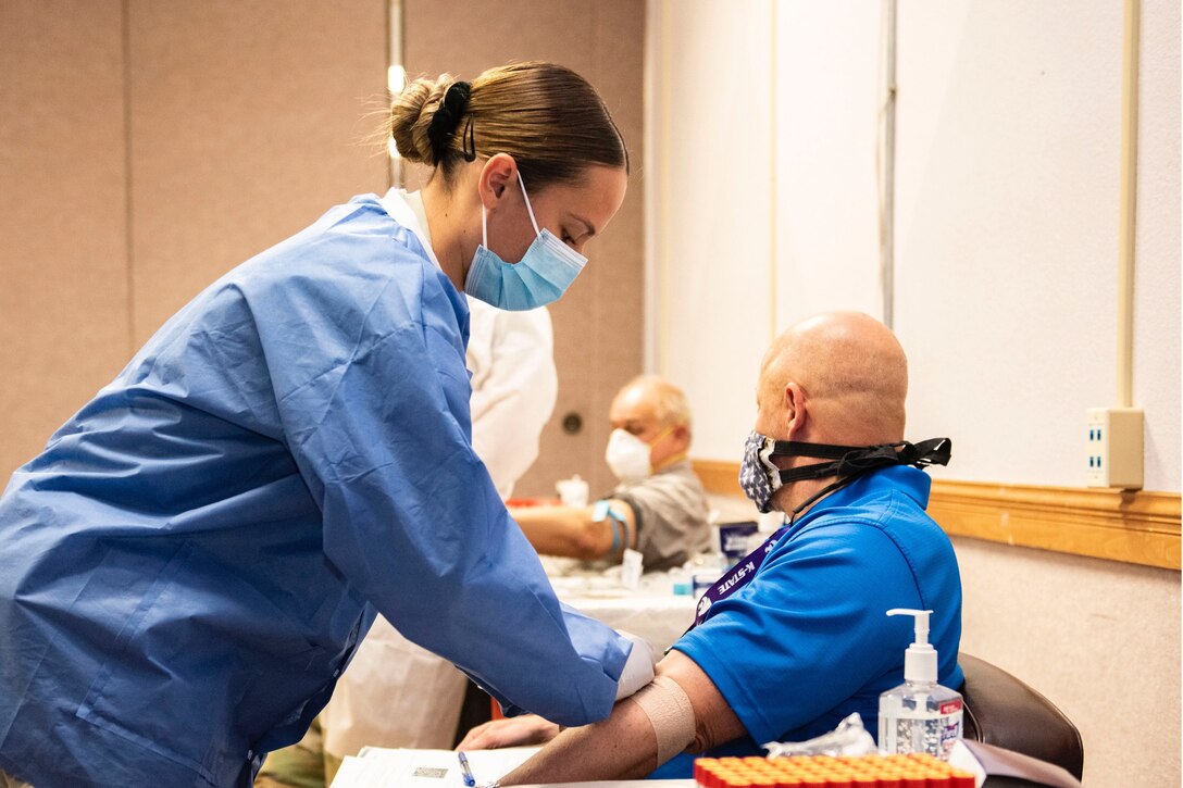 A technician wearing a mask and gloves wraps a bandage around a patient’s arm.