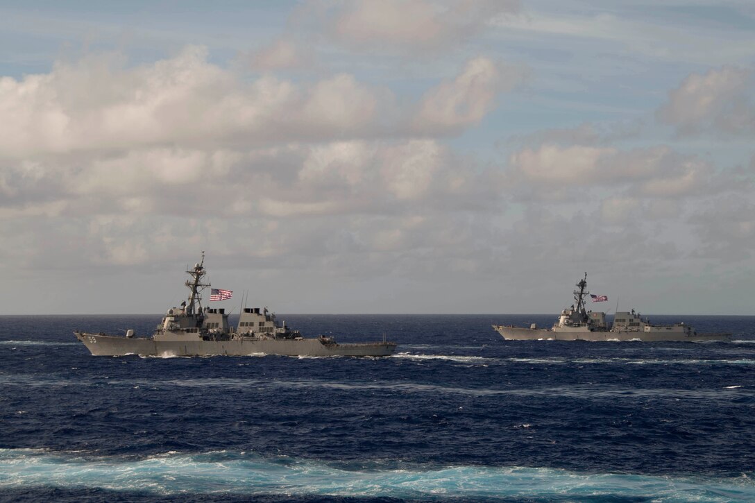 Navy ships travel a body of water.