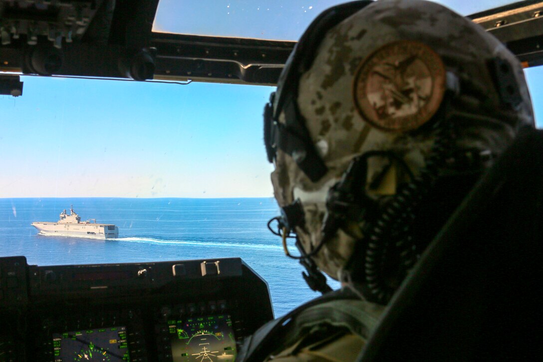 A pilot looks an aircraft cockpit at a ship in the water below.