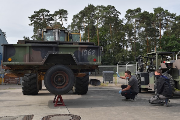 Two mechanics kneeling next to a trailer on a forklift.