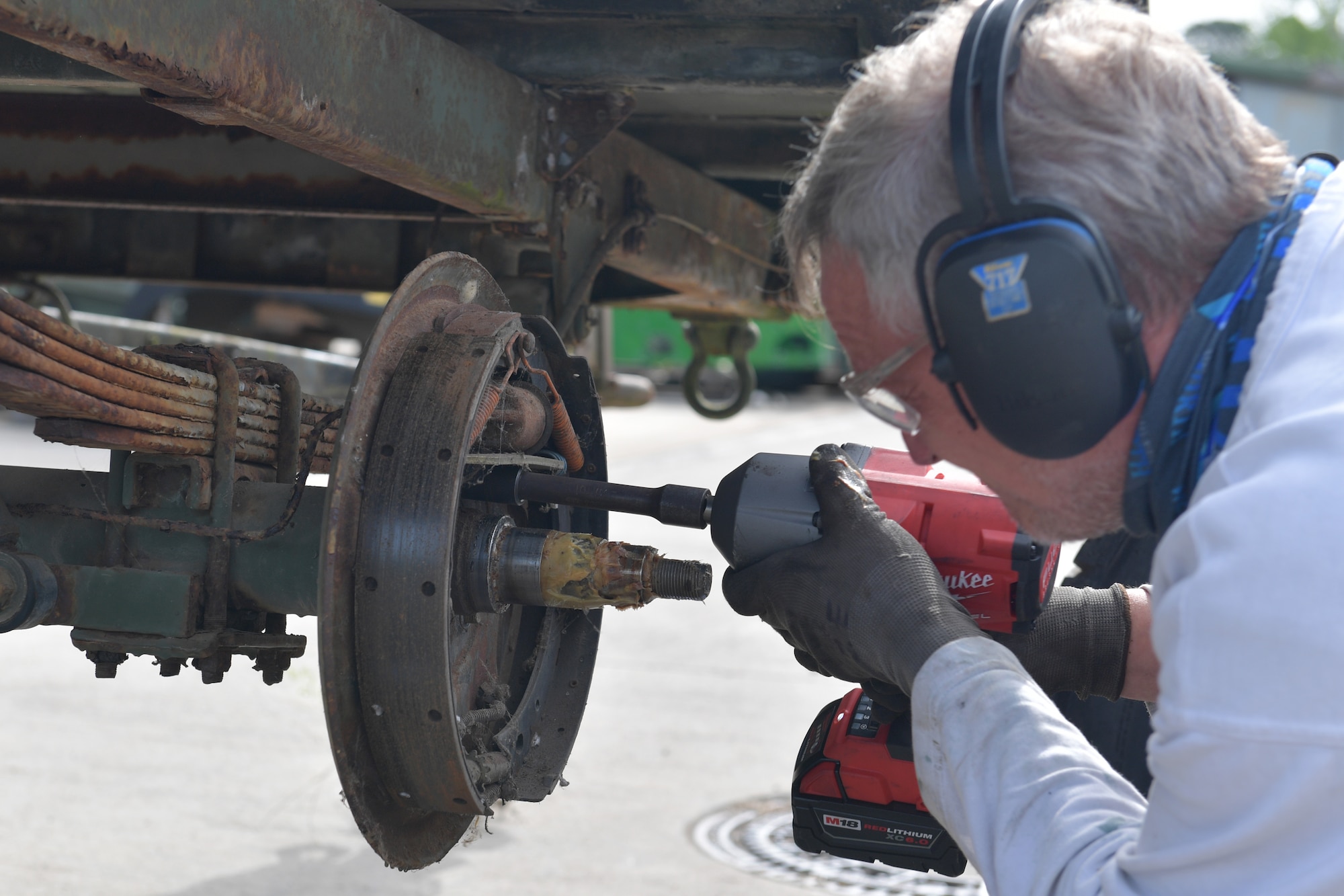 A mechanic working on a brake assembly with a power drill.
