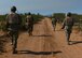 Four Air Force Airmen walk on a dirt road toward a small village made to simulate an austere location